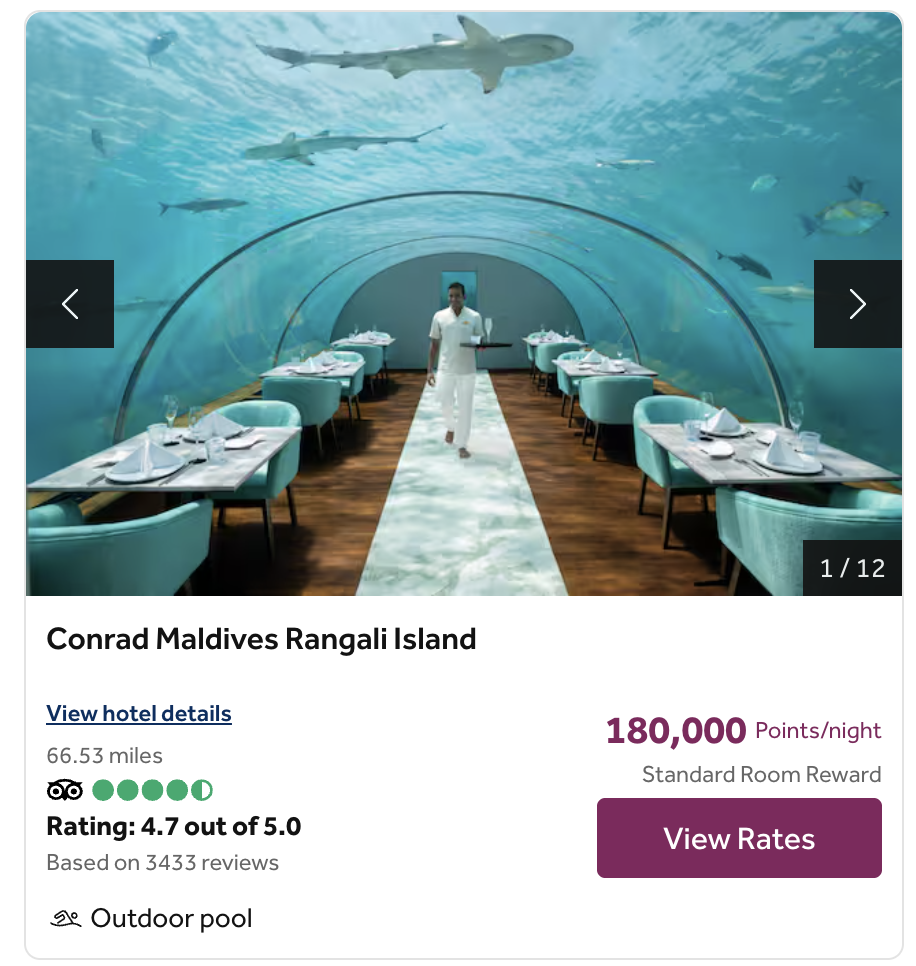 A waiter walks inside an underwater restaurant with glass walls and ceiling at Conrad Maldives Rangali Island, where not all points are equal—each table offers a unique view of fish and sharks swimming beside the elegantly set walkway.