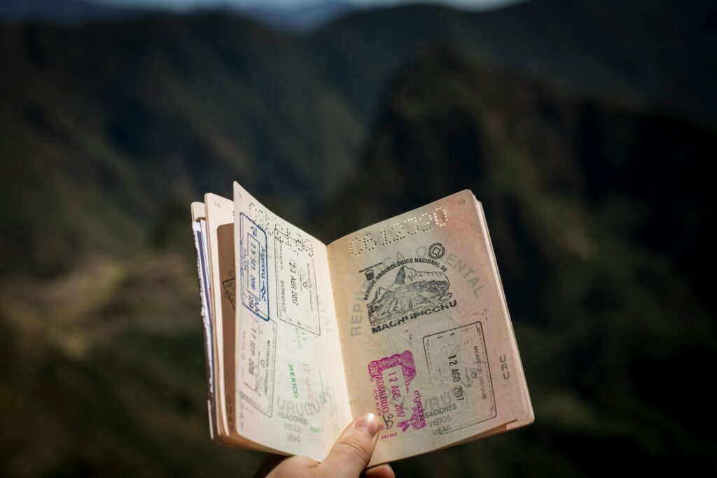 A hand holds an open passport filled with various stamps, including one labeled Machu Picchu, against a blurred mountain landscape—reminding us that not all points are equal when it comes to travel memories.