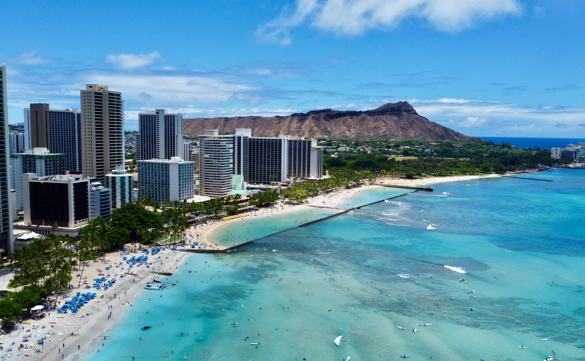 Aerial view of Waikiki Beach in Honolulu, Hawaii, with turquoise water, sandy beach, tall hotels, and Diamond Head crater—discover how to use rewards points for your stay under a blue sky with scattered clouds.