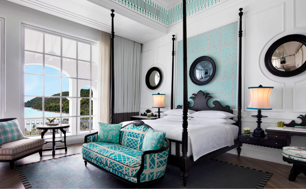 Elegant, bright hotel room with a four-poster bed, turquoise patterned sofa, large window with ocean and mountain view, two lamps, mirrors, and classic black-and-white decor.