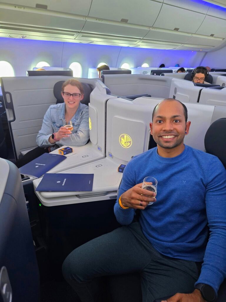 Ankit and Melissa smiling together in business class airplane seats.